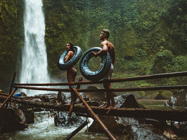 couples walking on a bridge each carrying tires with falls in the background